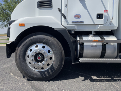 Front-left wheel and lower cab of a 2026 Mack MD6 truck showing tire, rim, fender, steps, and cab doors with badges and a DEF sticker.