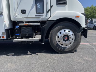 Mack MD6 front wheel area showing tire, wheel, and steps with engine-compartment components visible on the left.