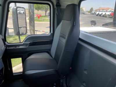 Interior cab view of a 2026 Mack MD6, single front seat with black upholstery, dashboard area visible through side window, exterior lot in background.