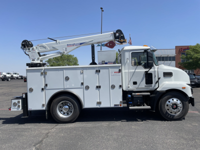 Service/utility truck with crane: white Mack MD6 utility body, mounted boom crane, compartments along side, cab and wheels visible.