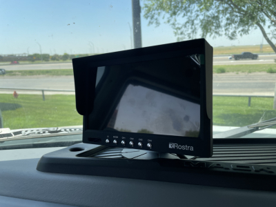 Rostra dashboard monitor on Mack MD6 cab dash with reflective screen, control buttons visible beneath screen.