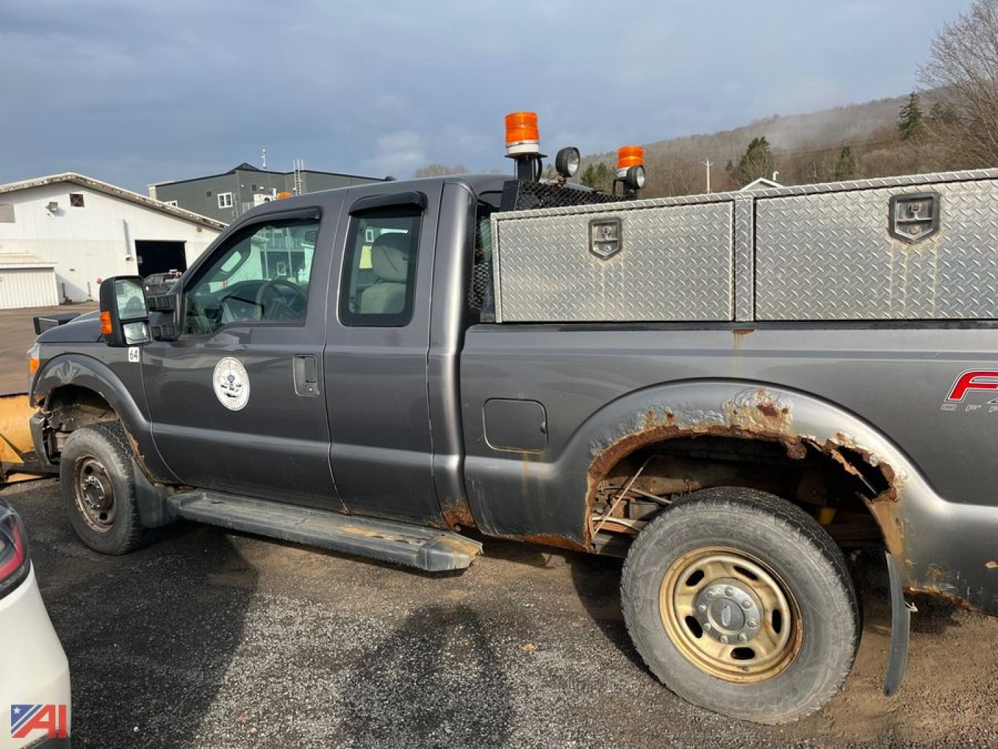 Ford F-250 Super Duty extended cab pickup with plow truck showing side view, rust on rear fender, dual orange beacon lights, and diamond-plate utility box in bed.