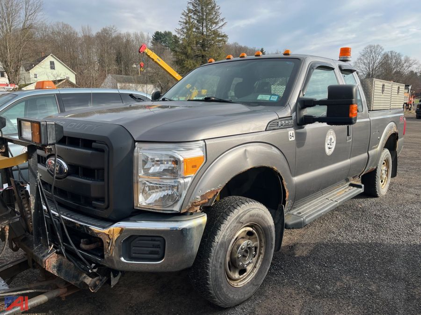 Ford F-250 Super Duty pickup with plow attachment in front, extended cab, gray exterior, dual rear wheels, orange plow beacon lights, utility decals on doors.