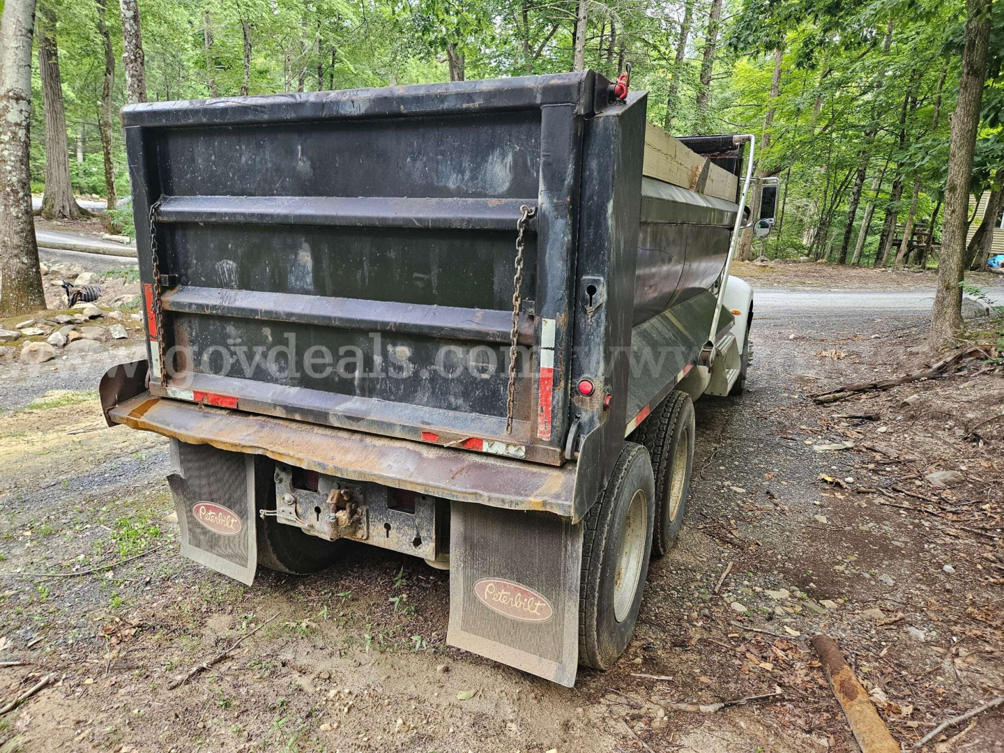 Dump truck rear view showing Peterbilt 335 dump bed, dual rear wheels, mud flaps, and taillights.