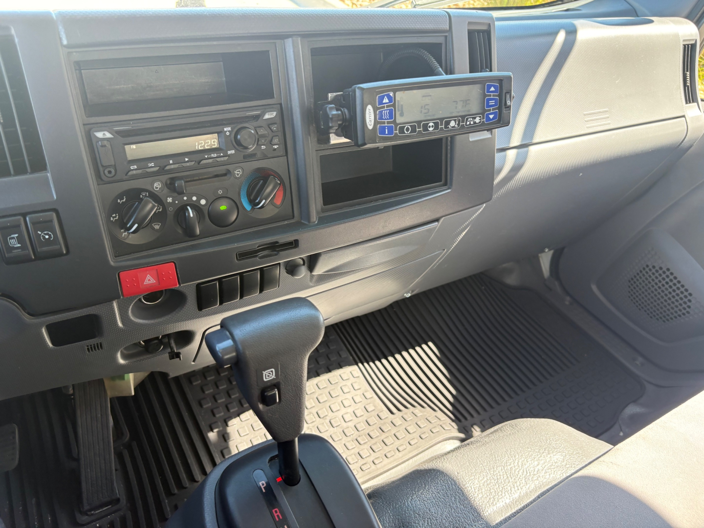 Dashboard view of a 2020 Chevrolet W4500 refrigerated truck shows steering column, climate controls, radio, and a mounted digital device with blue display; floor mat and gear selector visible.