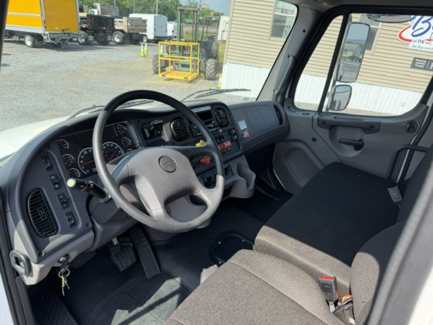 Truck cab interior showing steering wheel, dashboard, and front seats in a Freightliner M2-106 cab; gauges and controls visible on dash.