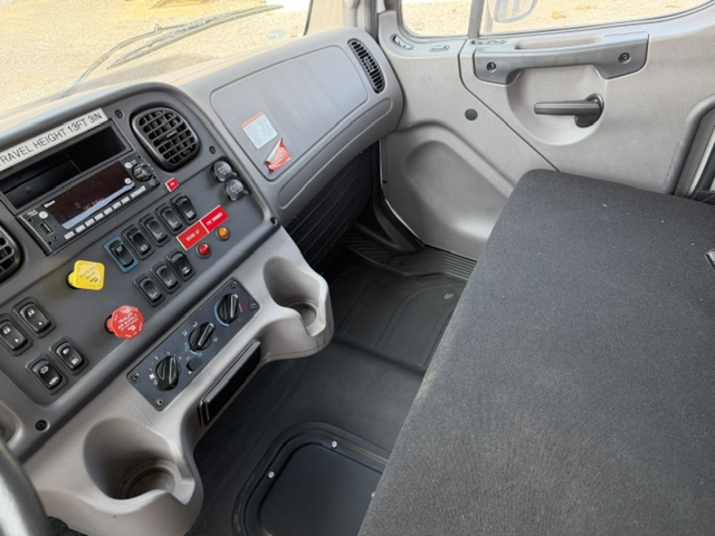 Cabin interior of a Freightliner M2-106 showing dashboard with control switches, steering wheel, gear area, and seating