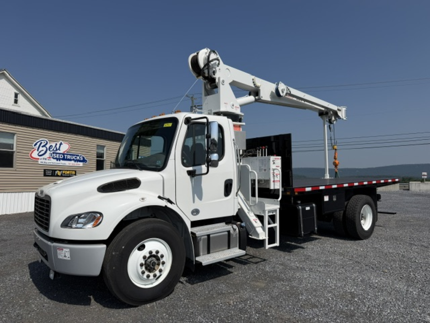 Freightliner M2-106 crane truck side view showing boom crane arm and white cab with lift controls.