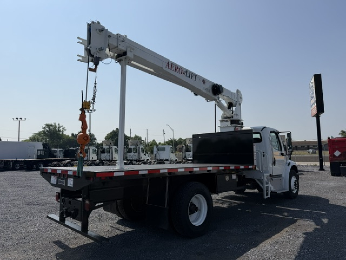 Truck-mounted crane on a white Freightliner M2-106 bed with a folding crane arm labeled ALRO-AFT, extended over the rear with rigging; VIN plate and stock number visible in background.