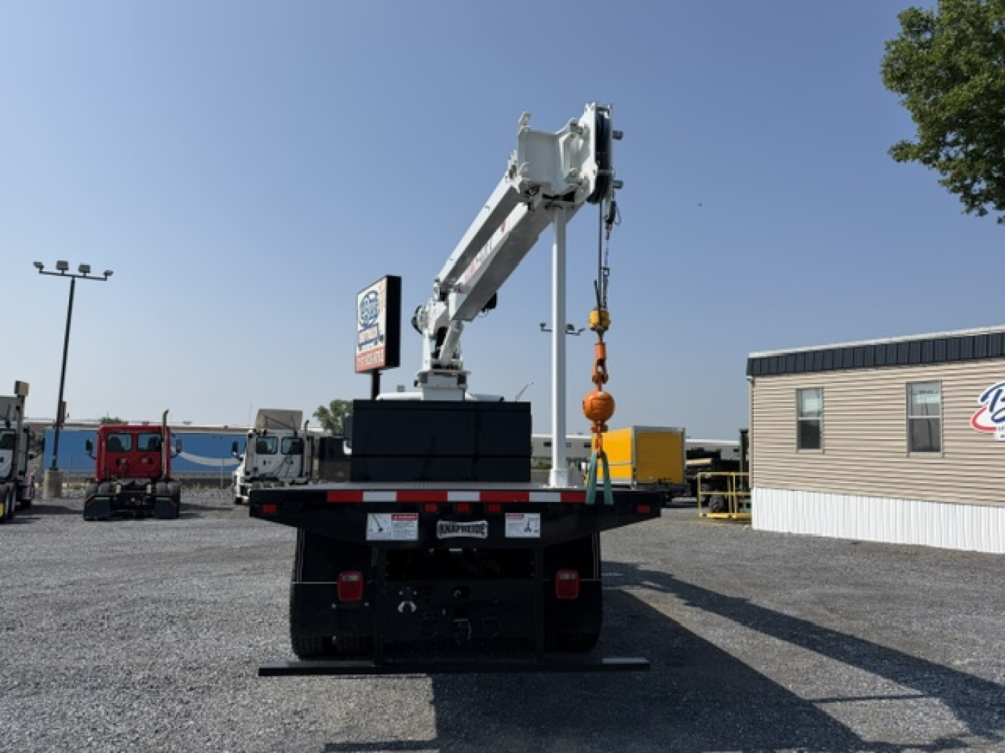 Truck bed with crane boom mounted, rear view of 2023 Freightliner M2-106 crane truck showing hydraulic crane arm and hook against clear sky.