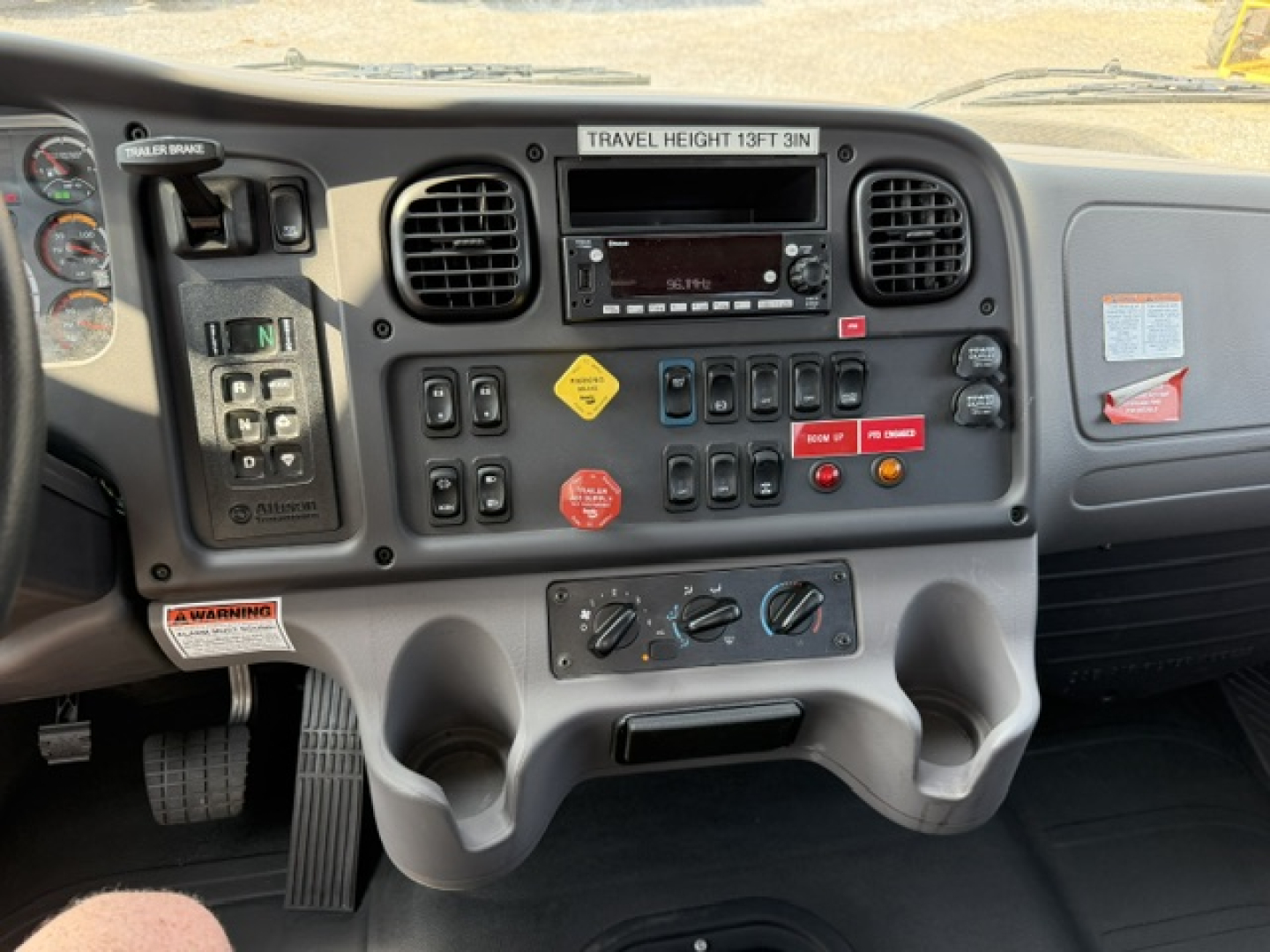 Dashboard of 2023 Freightliner M2-106 crane truck showing control switches, gauge cluster, vents, cup holders, and warning labels.