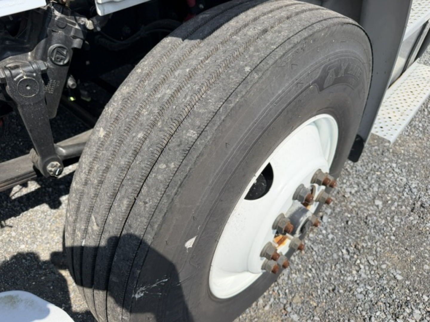Freightliner M2-106 wheel end showing front dual rear axles with tire and white steel wheel; visible lug nuts and hub; part of chassis and step area.