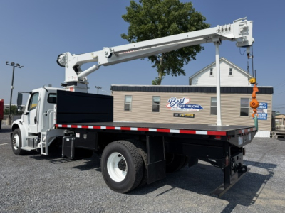Freightliner M2-106 truck with crane in-travel configuration showing long boom and hook in service bay.