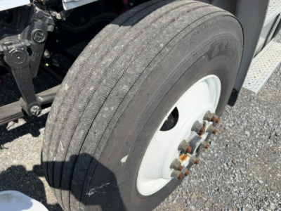 Freightliner M2-106 wheel end showing front dual rear axles with tire and white steel wheel; visible lug nuts and hub; part of chassis and step area.