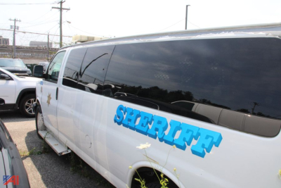 Chevrolet Express cargo van side view with large blue SHERIFF lettering on white body, reflective windows, parked on lot.