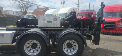 Kenworth T600 truck chassis with dual rear axles and mounted equipment; aluminum toolbox and gauges visible on the side; front cab area visible in background.