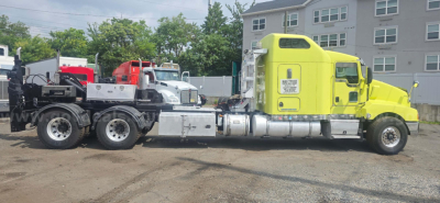 Kenworth T600 truck tractor with a bright yellow cab and chrome fuel tanks, attached to a tow trailer in a yard.