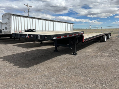 Flatbed trailer showing drop deck with dual rear axles and portable support legs.