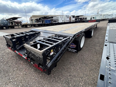 Trailer bed with wooden deck and black steel framework, TULY equipment label, rear ramp area, and drop deck trailer in a yard.