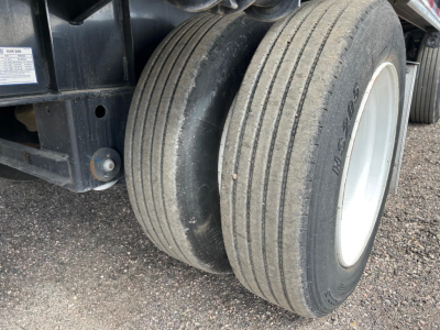 Dual rear axles with tires on a steel drop deck trailer; visible tire tread and sidewall markings reading 'DU-452' and other faint scripts.