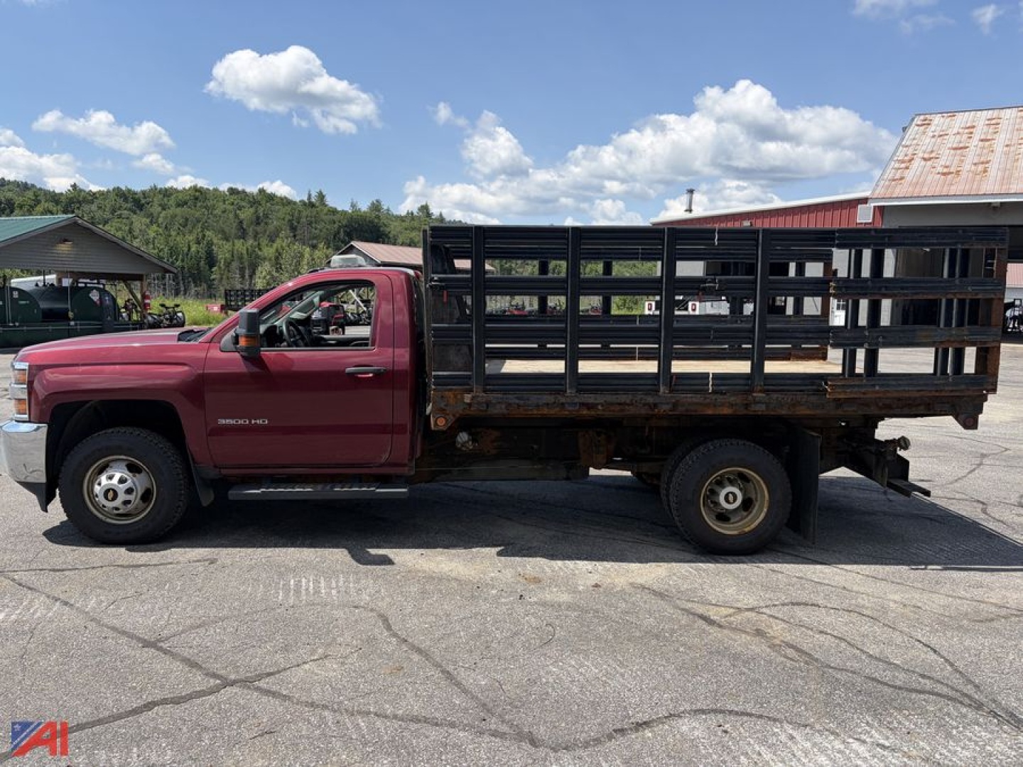 Truck side profile showing a 2015 Chevrolet Silverado 3500HD stake bed rack truck with a red cab and black metal flatbed rack.