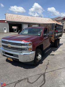 Chevrolet Silverado 3500HD rack truck with red cab and rusted flatbed in a lot; front chrome bumper; black grille; side mirrors; rack bed and open cargo area.