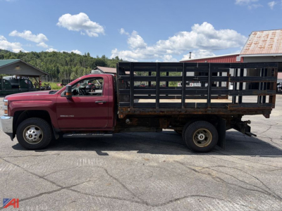 Truck side profile showing a 2015 Chevrolet Silverado 3500HD stake bed rack truck with a red cab and black metal flatbed rack.