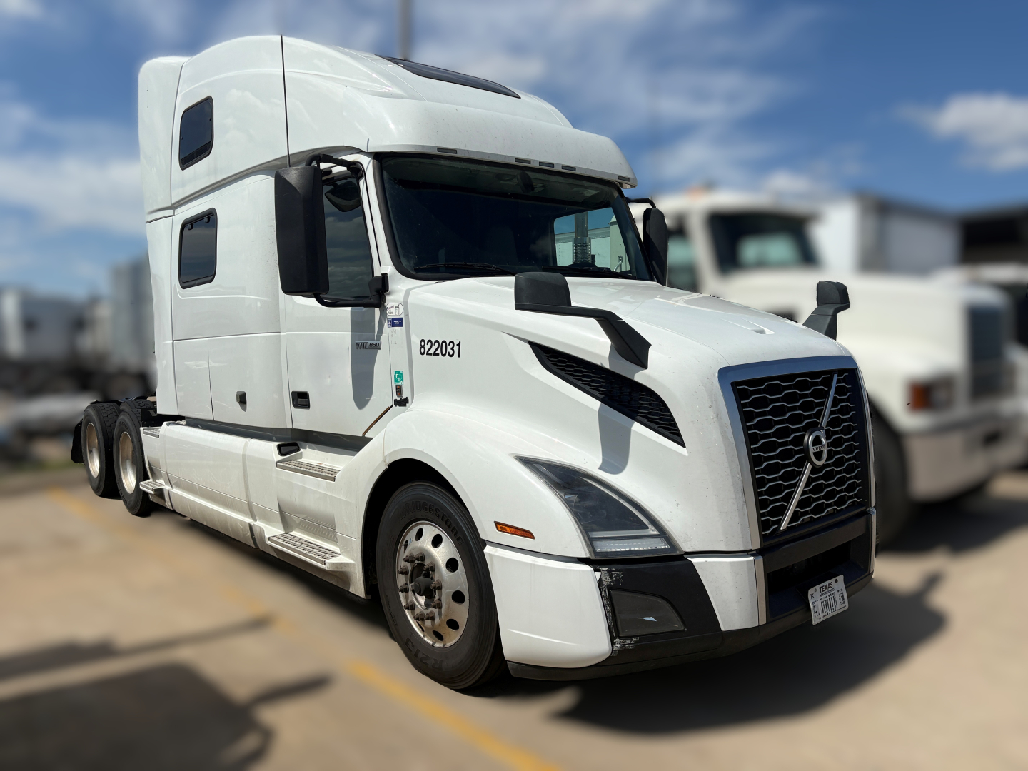Volvo VNL64T860 truck in white cab, front three-quarter view showing side sleeper, grille with Volvo emblem, and wheel tags.