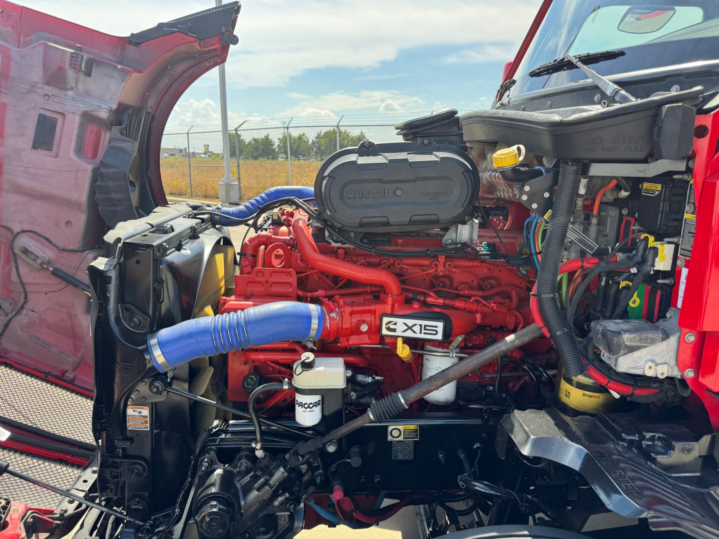 Kenworth T680 engine bay showing Cummins X15 engine and blue intercooler hose and various red components.