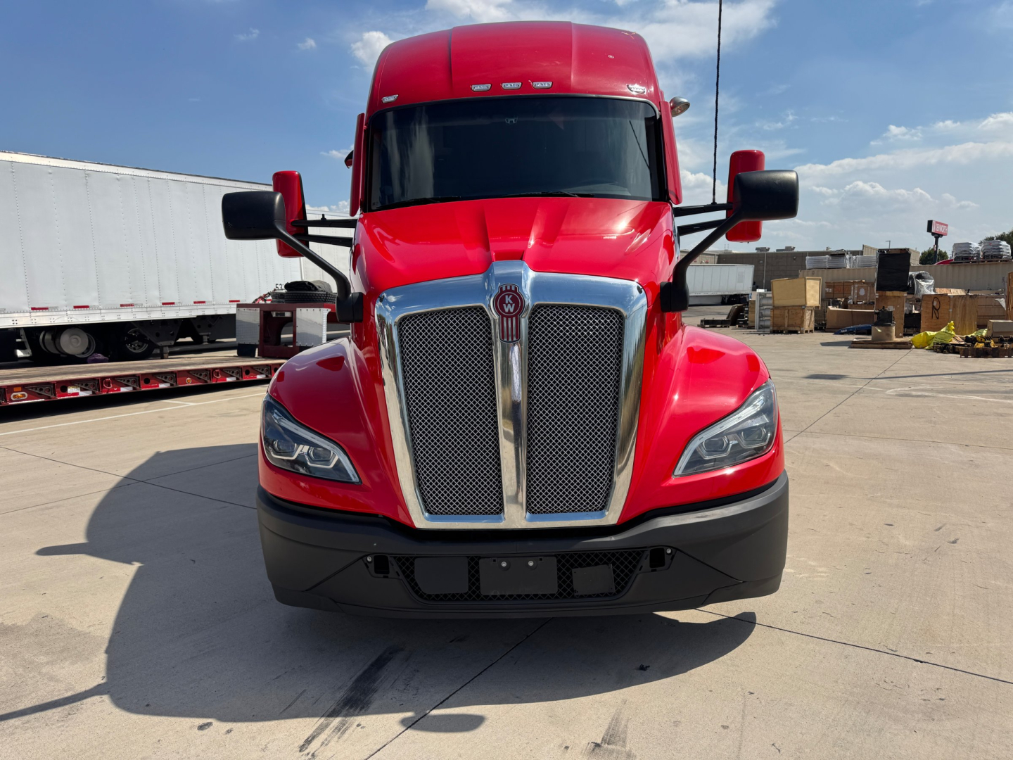 Kenworth T680 front view showing bold chrome grille and red cab with black bumper and mirrors.