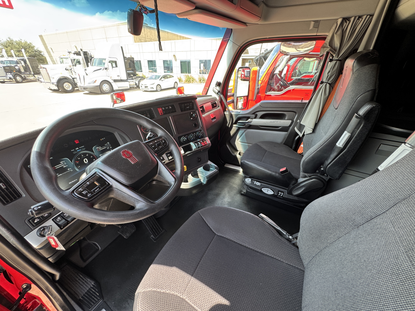 Kenworth T680 interior cab view showing steering wheel with Kenworth emblem, dashboard, driver seat, and center console.