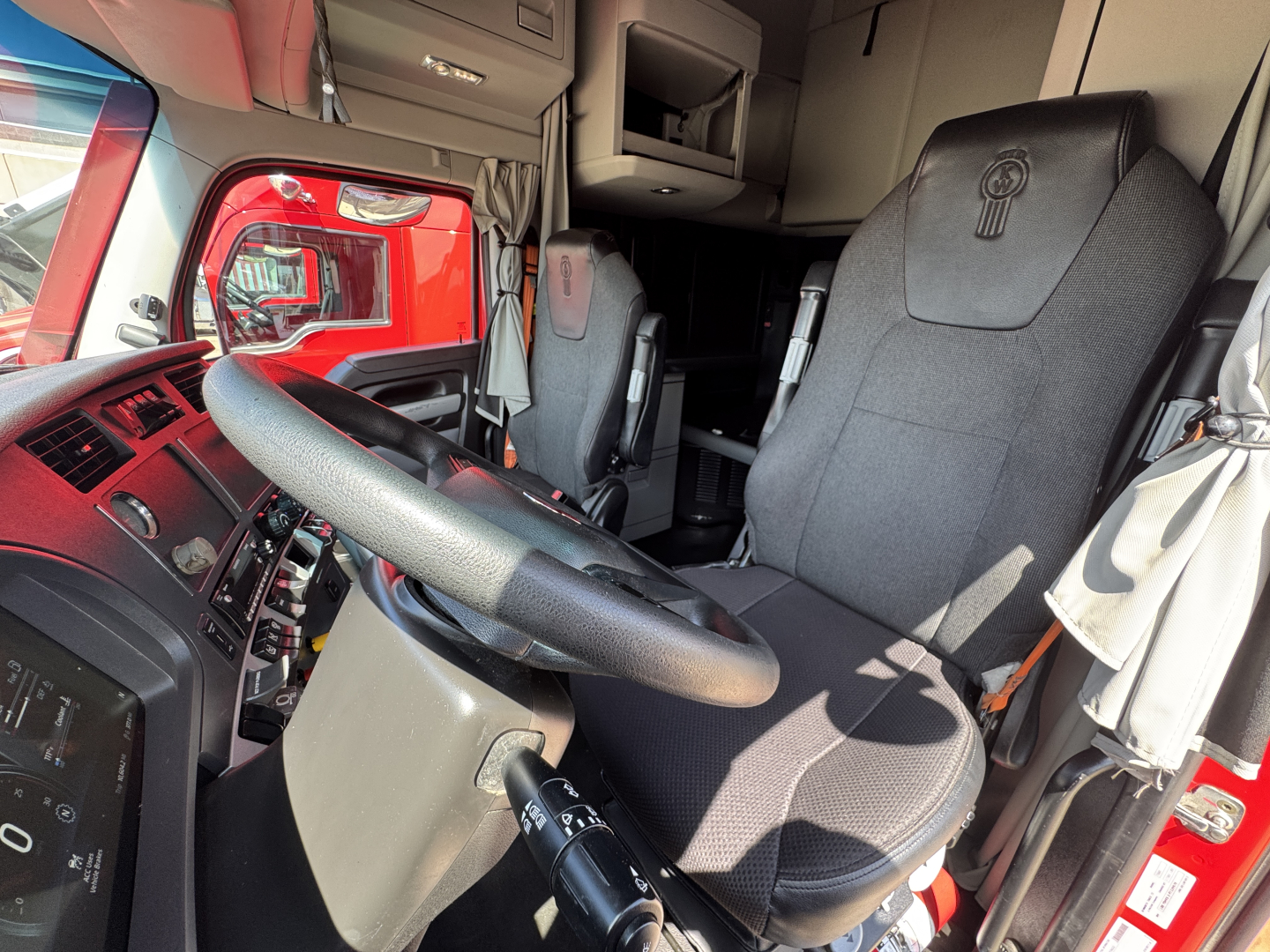 Kenworth T680 truck interior showing steering wheel, driver seat, dashboard, and cab area with other seating and storage compartments visible.