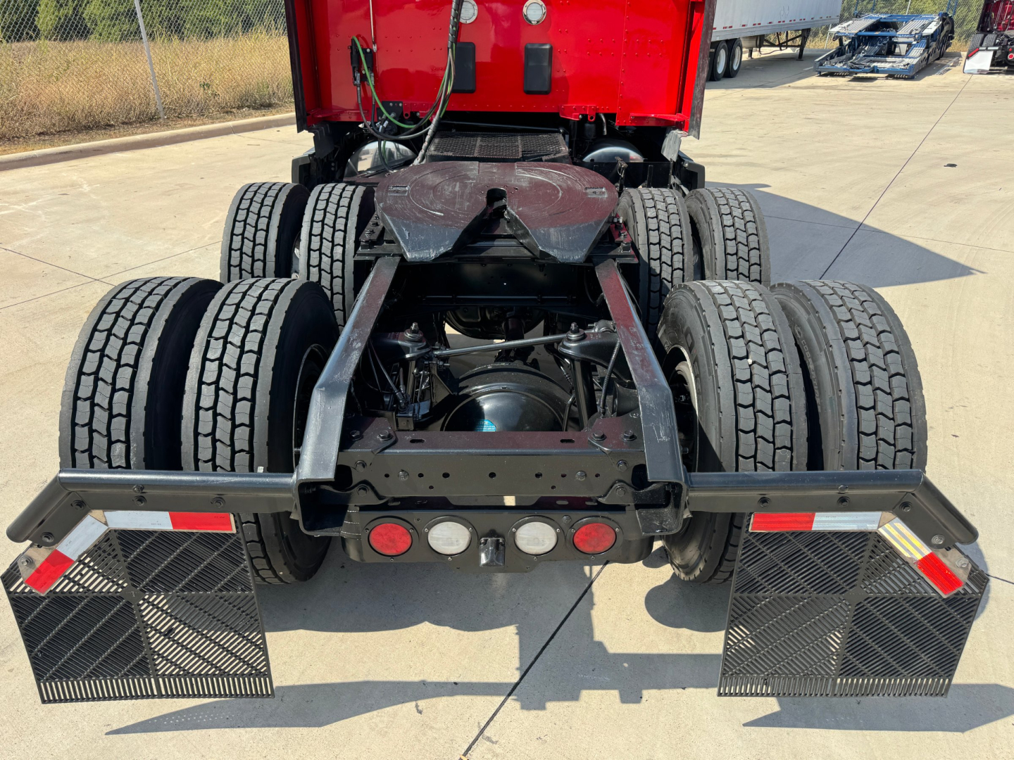 Kenworth T680 chassis rear view showing dual rear axle and fifth wheel with mudflaps and rear lights.