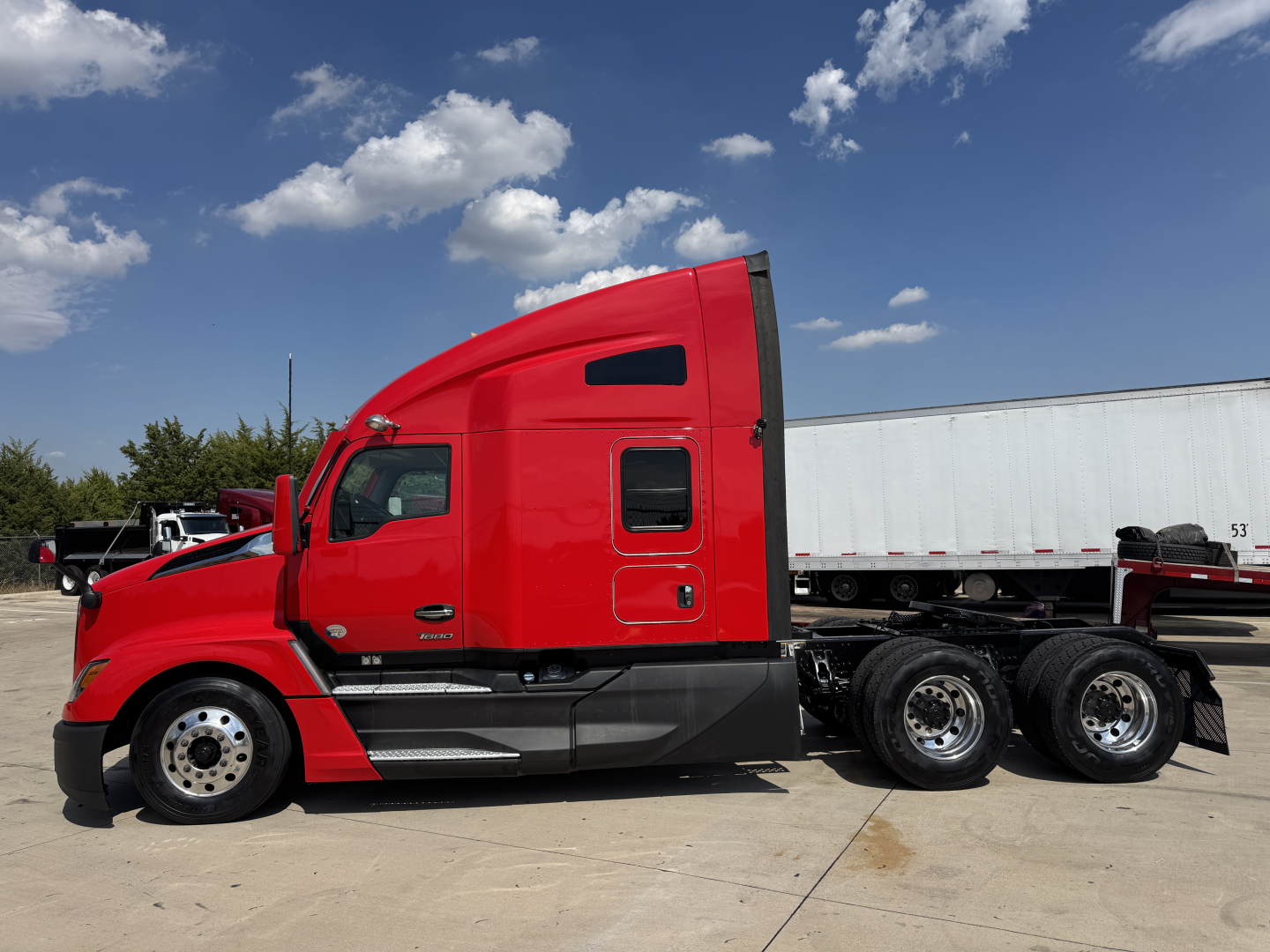 Kenworth T680 tractor in red side profile view showing sleeper cab, truck wheels, and trailer connection with blue sky.