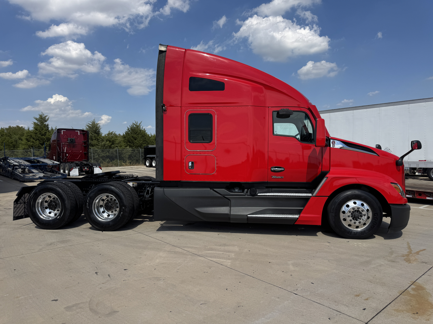 Kenworth T680 sleeper cab truck side view showing red tractor with black lower cab and wheel arches.
