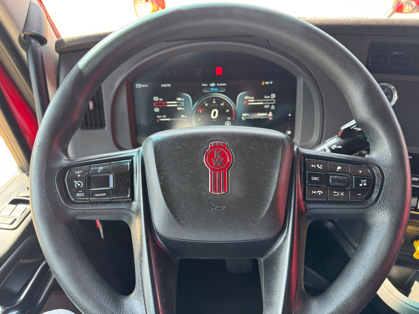 Kenworth T680 dashboard with steering wheel center emblem and digital gauges visible, showing steering wheel controls on both sides and a digital instrument cluster.
