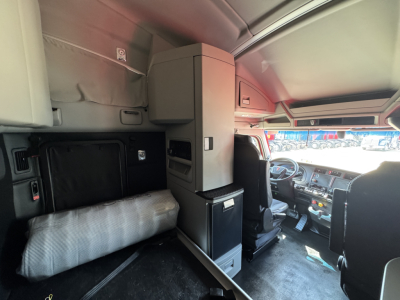 Kenworth T680 cab interior showing sleeper area with pillow, storage cabinet, and driver seat; dashboard and windshield visible.