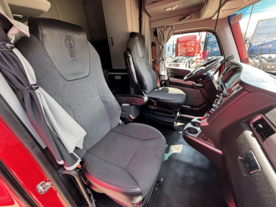 Truck cab interior of a 2023 Kenworth T680 showing grey fabric seats, dashboard, steering wheel, and center console from the passenger side.