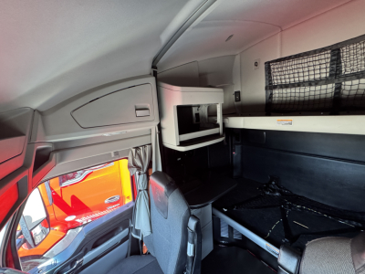 Kenworth T680 truck interior cab area showing sleeper bunk with storage shelf and netting, driver seat, and windowed partition.
