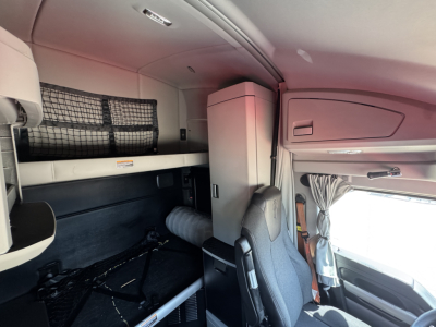 Kenworth T680 sleeper cab interior showing upper bunk, storage cabinet, and driver seat area with window and curtains.