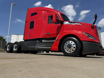 Kenworth T680 truck in red, side view showing cab with sleeper, three rear axles, and chrome fuel tanks. No visible text on the truck panels.