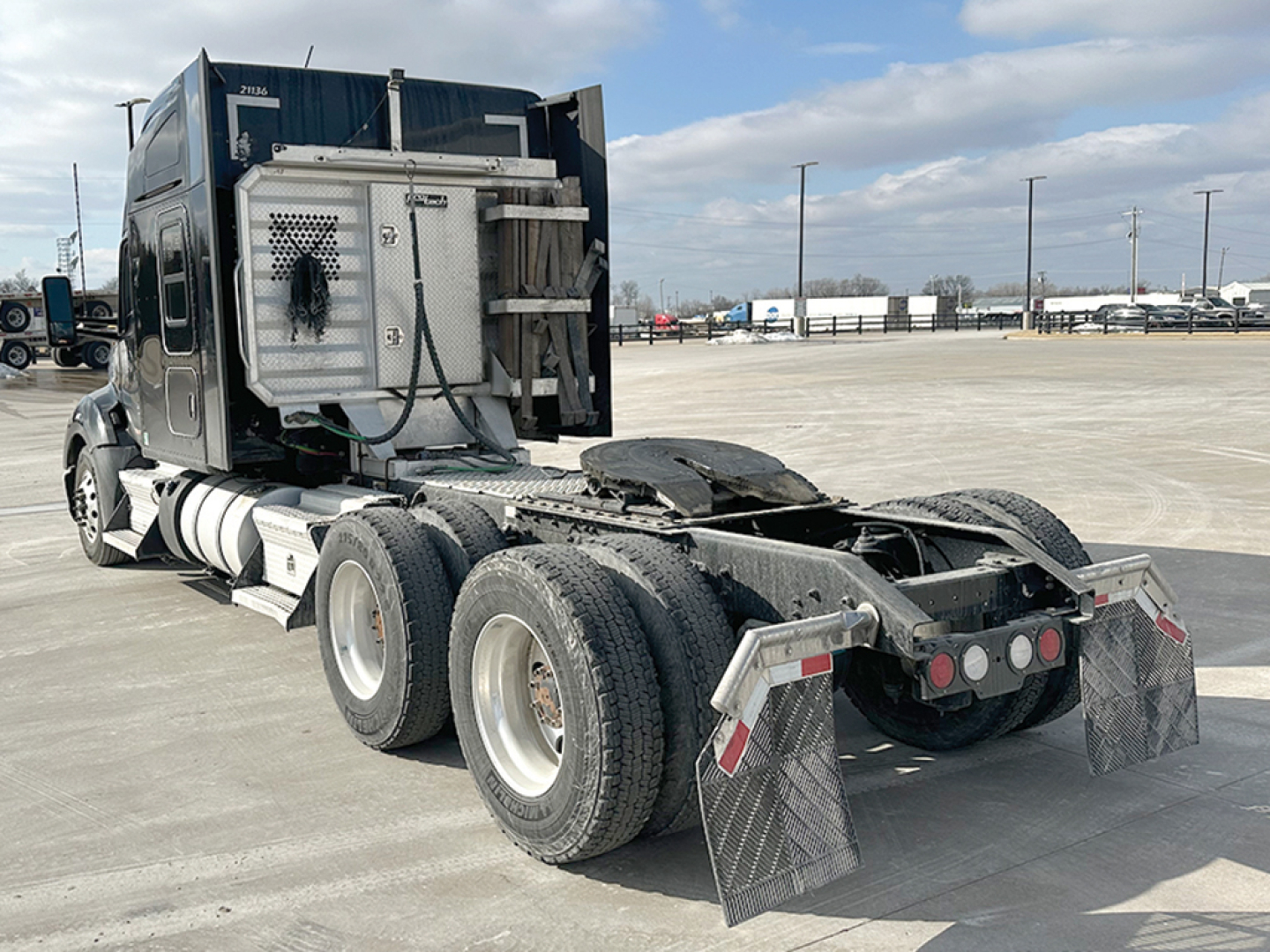 Kenworth T680 tractor with sleeper cab, rear view showing fifth wheel and dual rear axles, exhaust stack visible, spare attachment area and mud flaps.