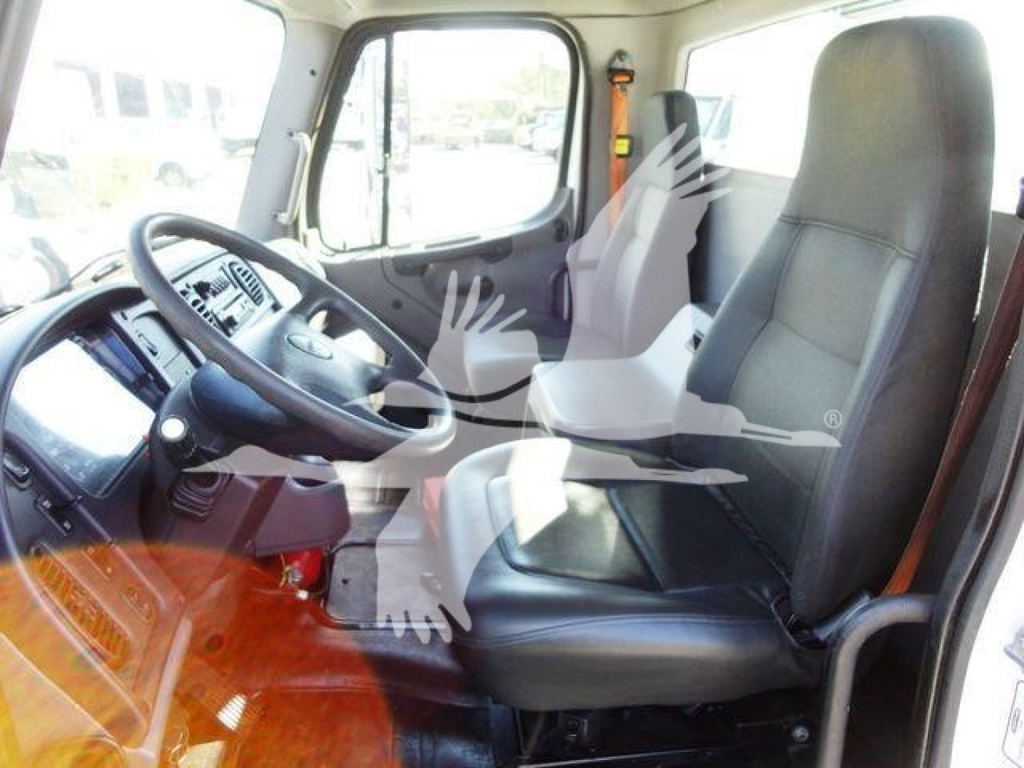 Cab interior of a Freightliner Business Class M2 106 showing steering wheel, driver seat, and dashboard with mesh window reflections.