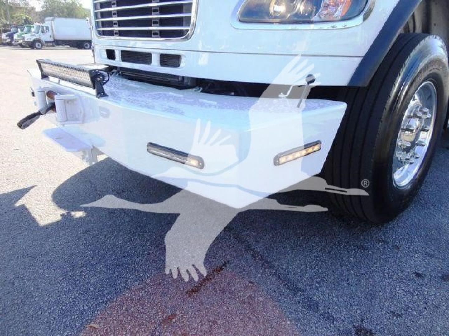 Front bumper and right front section of a 2012 Freightliner Business Class M2 106 winch truck showing bumper with integrated side marker lights and chrome wheel.