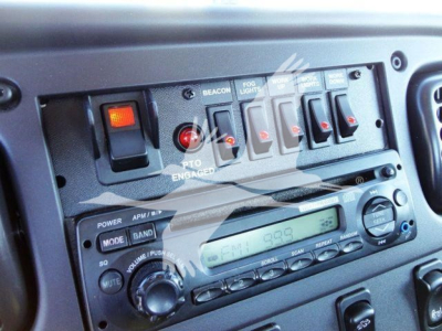 Dashboard controls and radio panel of a Freightliner M2 106 truck showing switches labeled BEACON, FOG LIGHTS, HAZARD, and radio with display and knobs.