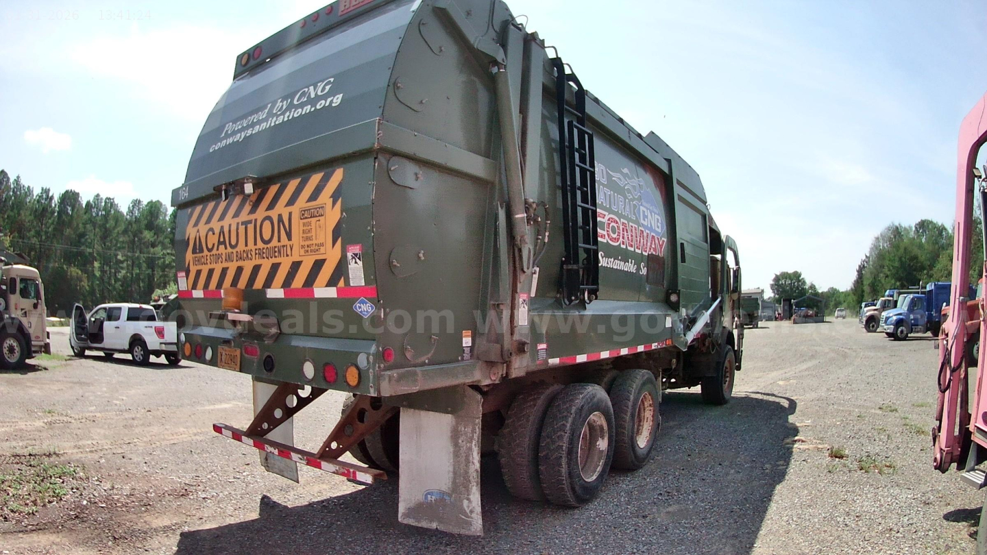 Rear view of a 2015 Mack MRU613 refuse truck showing cargo body and triple-axle rear with caution decals and CGA logo