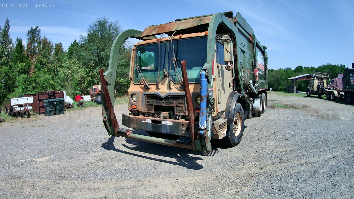 Mack MRU613 garbage truck side view showing front with hydraulic arms and rear compactor. Visible VIN tag area and exterior wear.