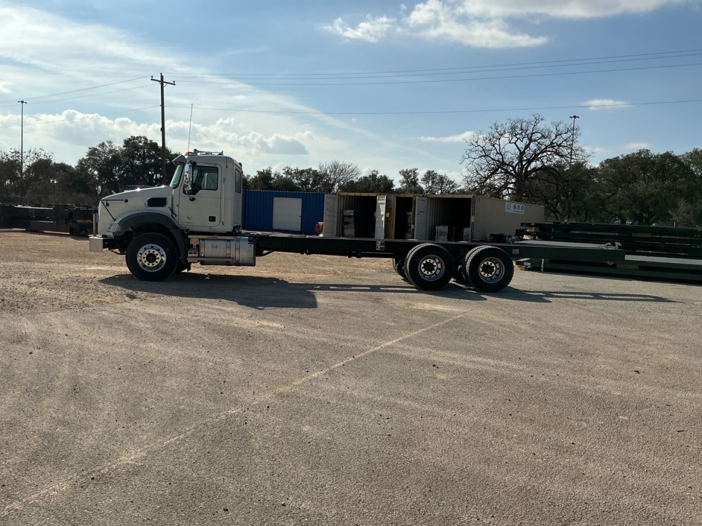 Truck cab and long flatbed crane chassis in an empty lot showing side view with Mack GR64B cab and crane equipment.