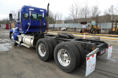Kenworth T660 conventional day cab tractor in blue, side view showing rear dual axle and fifth wheel, with white mudflaps.