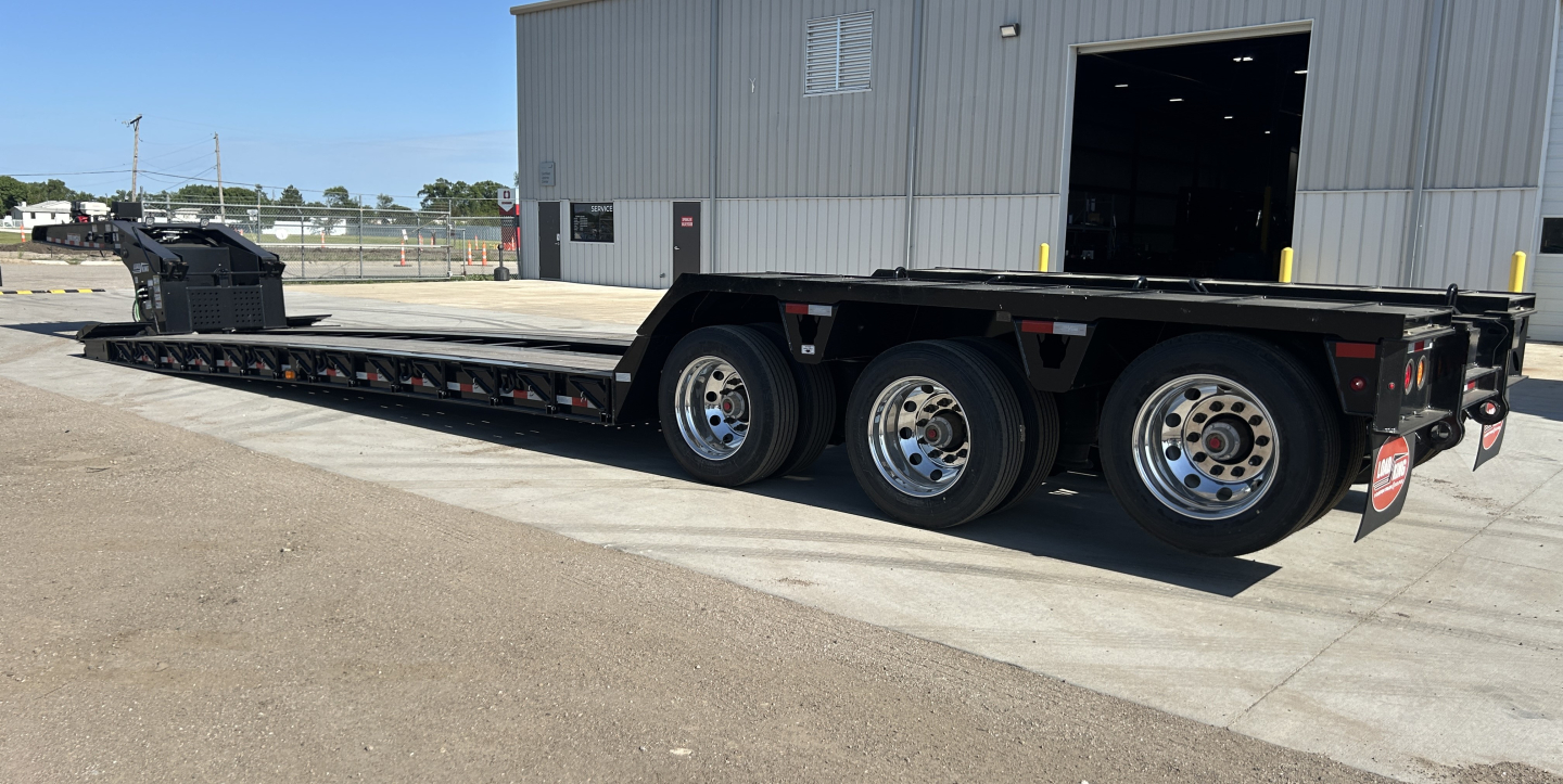 Trailer showing Load King lowboy with long flatbed and multiple axles, black frame, alloy wheels, and ramp at rear, side rails and wheel wells visible.